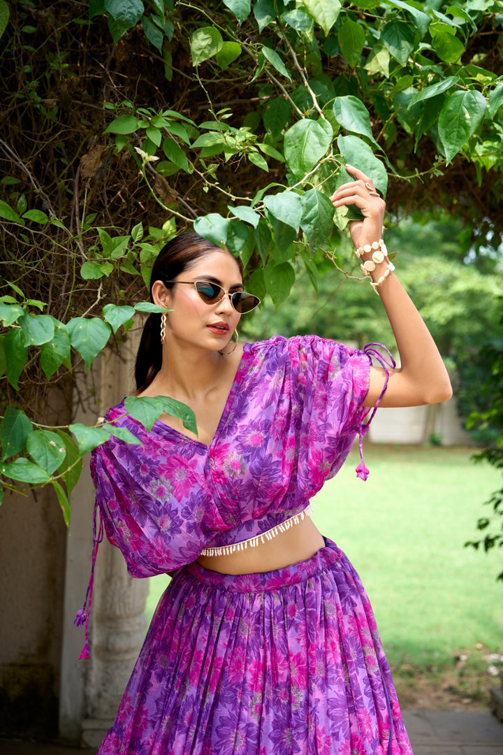 Purple Chiffon Dhavani Set includes a stitched chiffon lehenga with floral print, featuring a drawstring and zip closure, and a comfortable waist support up to 42 inches. The lehenga is 41 inches long with a 9-meter flair and a micro cotton inner lining. The matching chiffon blouse is fully stitched with floral print and pearl accents, sized to fit 36 to 42 inches comfortably. The set contains both the lehenga and blouse, offering a complete traditional outfit with elegant detailing.