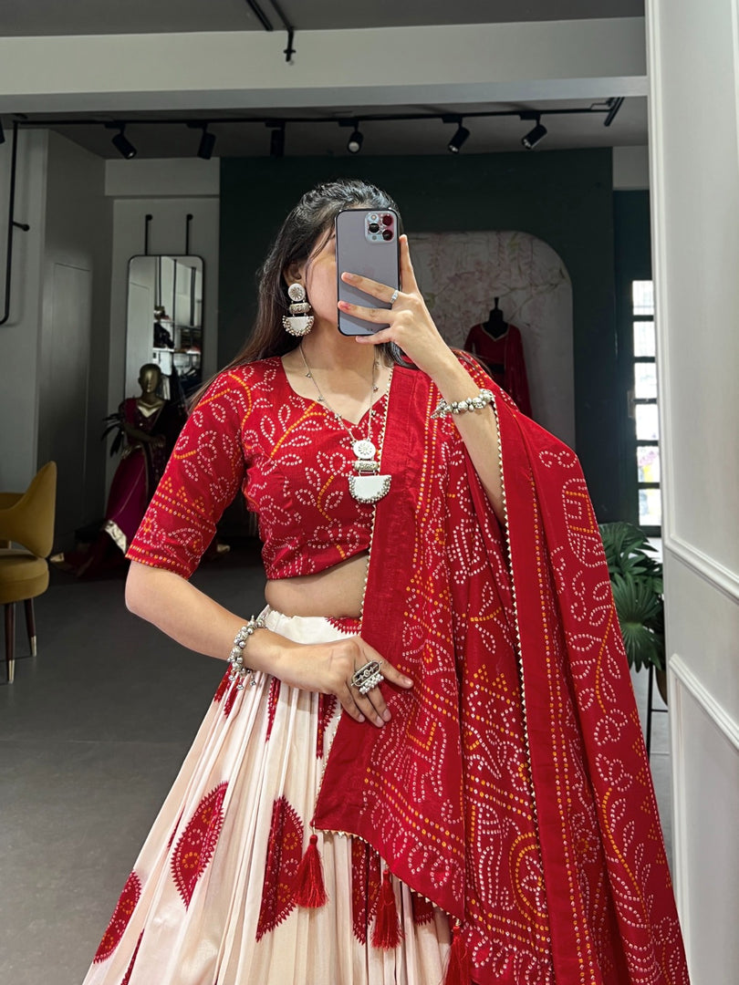 Bright red Bandhej lehenga in luxurious tussar silk , Red bridal wear lehenga with Bandhej print and lace border , Festive red color lehenga with handmade tassels and flair , Designer red Tussar silk lehenga for wedding occasions.