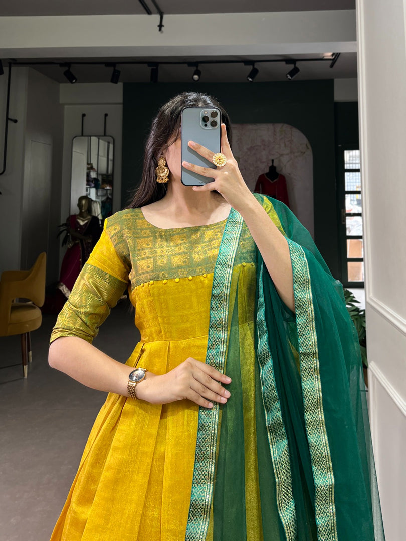 Yellow Color Kanjivaram Anarkali Zari Weaving Work With Price and Online Shopping Price Under 1500 .  Elegant Kanjivaram stitched gown with zari weaving, silk lining, and 3.5-meter flair. Paired with a plain net dupatta featuring a lace border. Perfect for festive occasions.